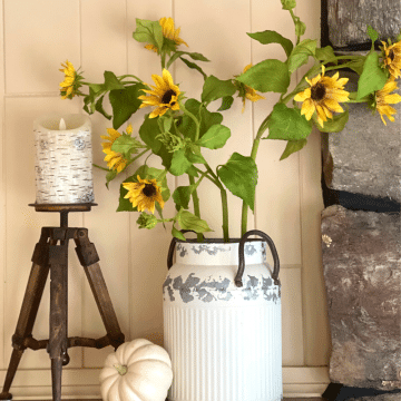 Fall mantle decor with milk can filled with pretty sunflowers and a candle and white pumpkin.