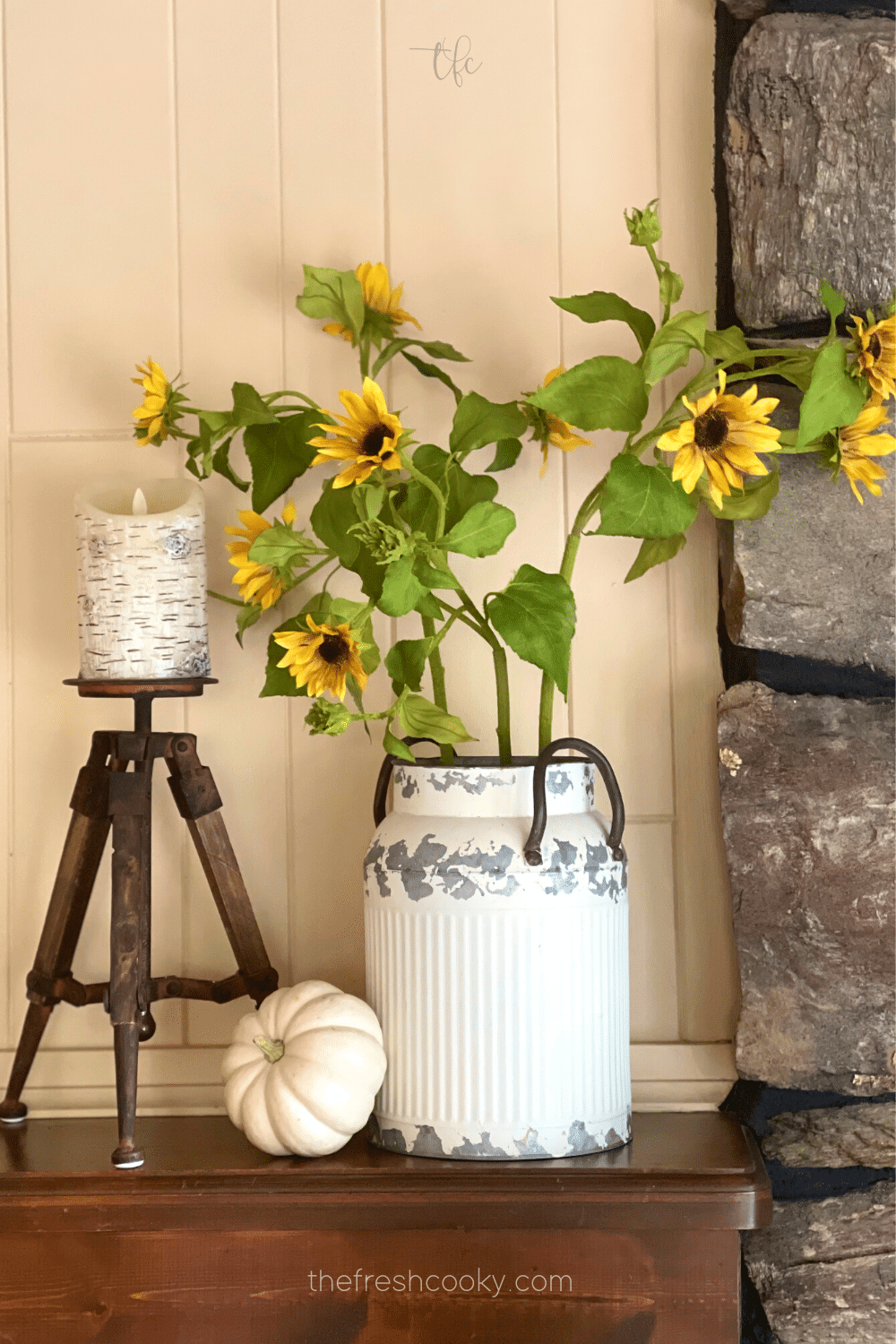 Fall mantle decor with milk can filled with pretty sunflowers and a candle and white pumpkin.