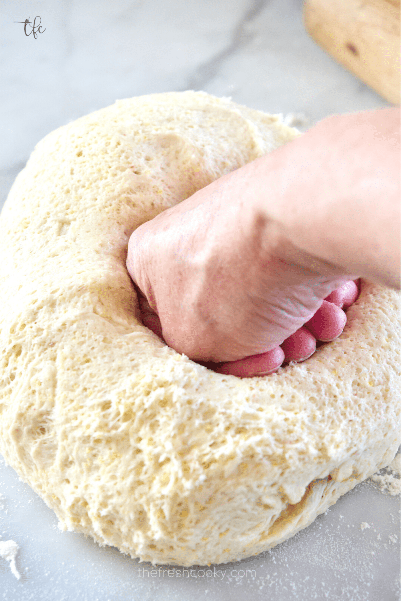 Handing punching down deep dish pizza dough on floured surface. 