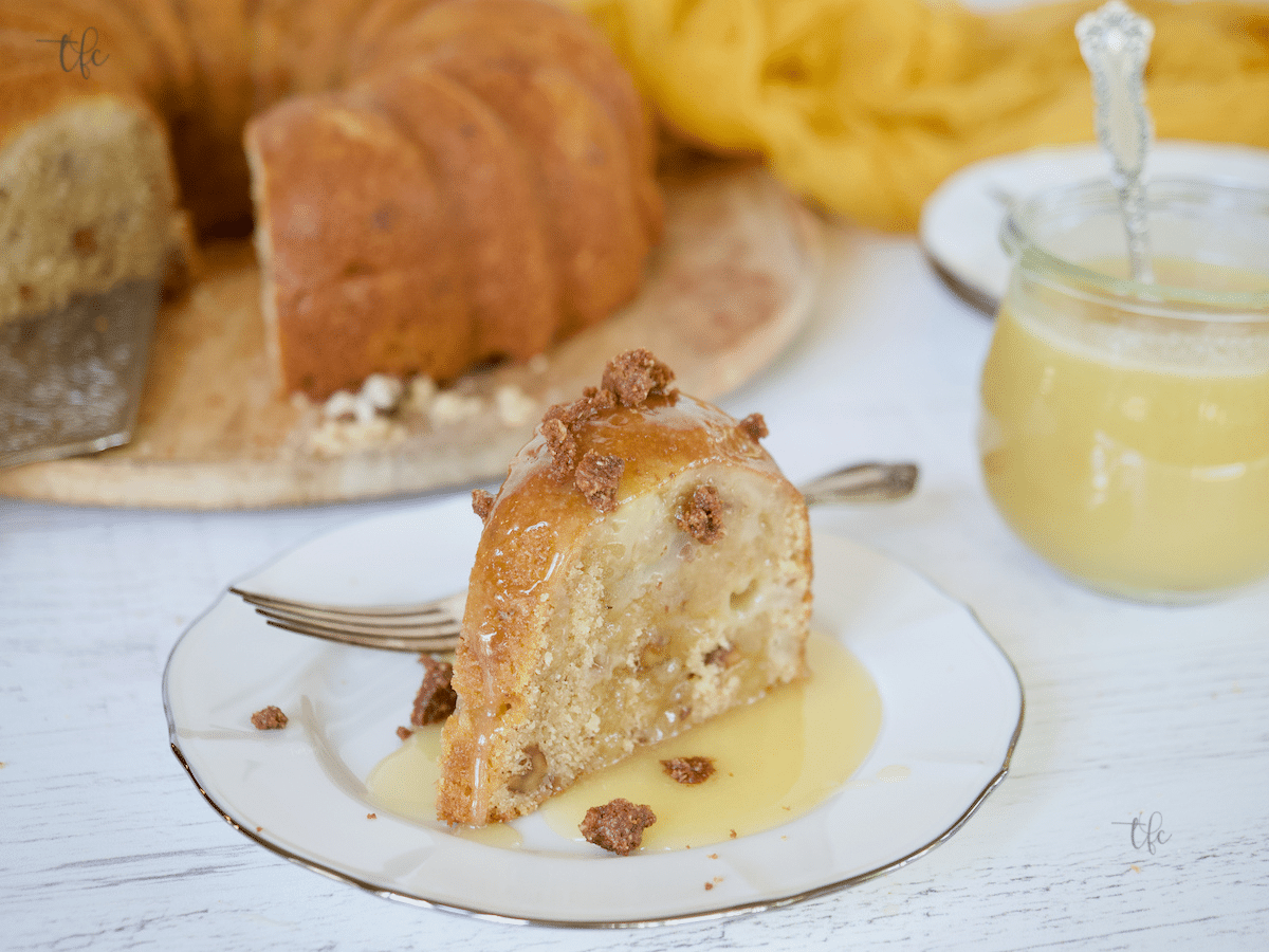 Slice of pear cake on a pretty plate dripping with vanilla butter sauce and graham cracker crumble on top.