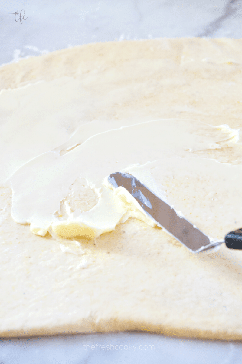 Spreading soft butter onto deep dish pizza dough.