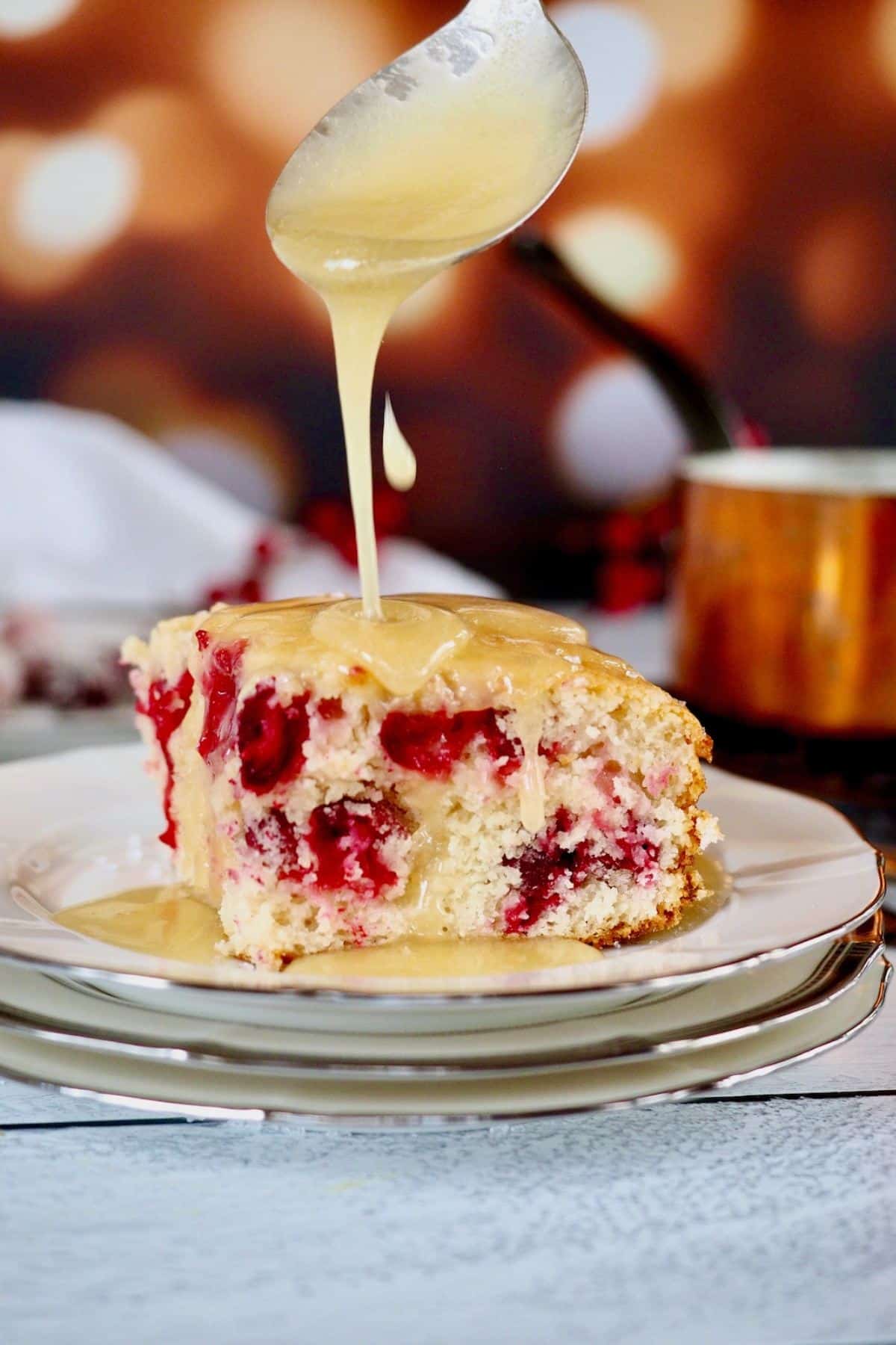 Vanilla butter sauce being poured over cranberry Christmas cake.