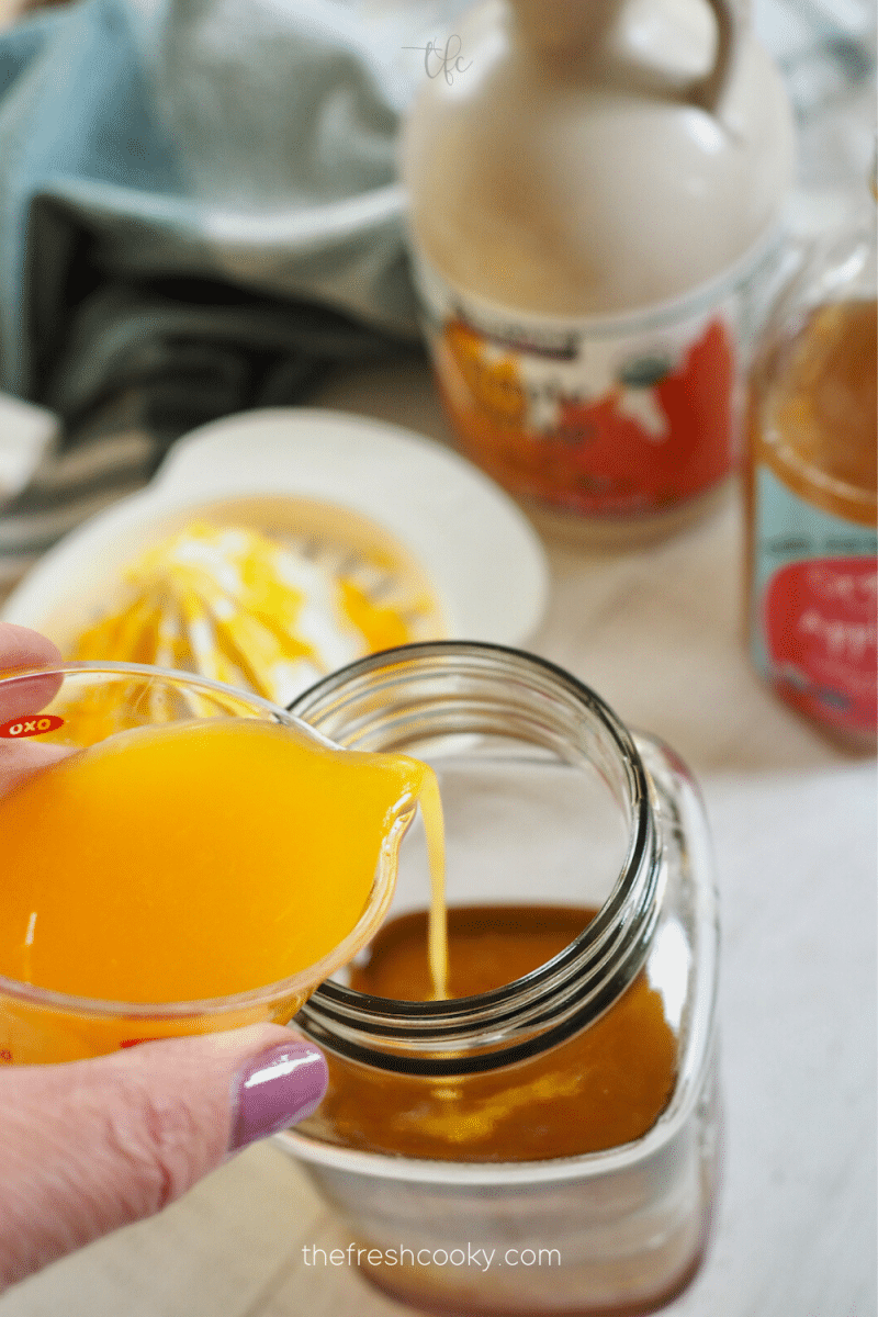 Adding orange juice to mason jar for apple cider vinaigrette.