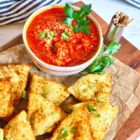 Air Fryer Ravioli on a wooden board with a bowl of marinara sauce and toothpicks for an easy appetizer.