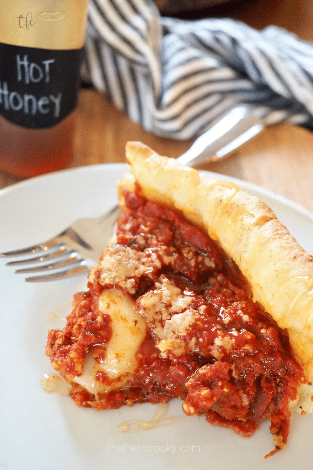 Image of slice of deep dish Chicago style pan pizza on plate with a fork and hot honey behind.