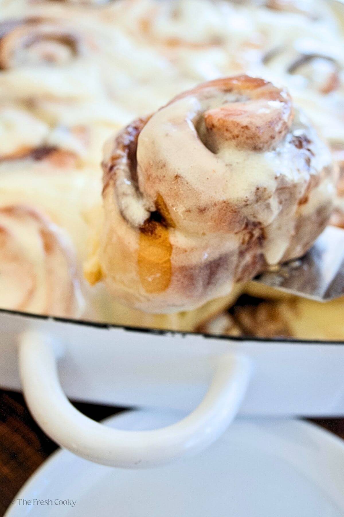 Pulling a frosted cinnamon roll out of the pan with a sptaula. 