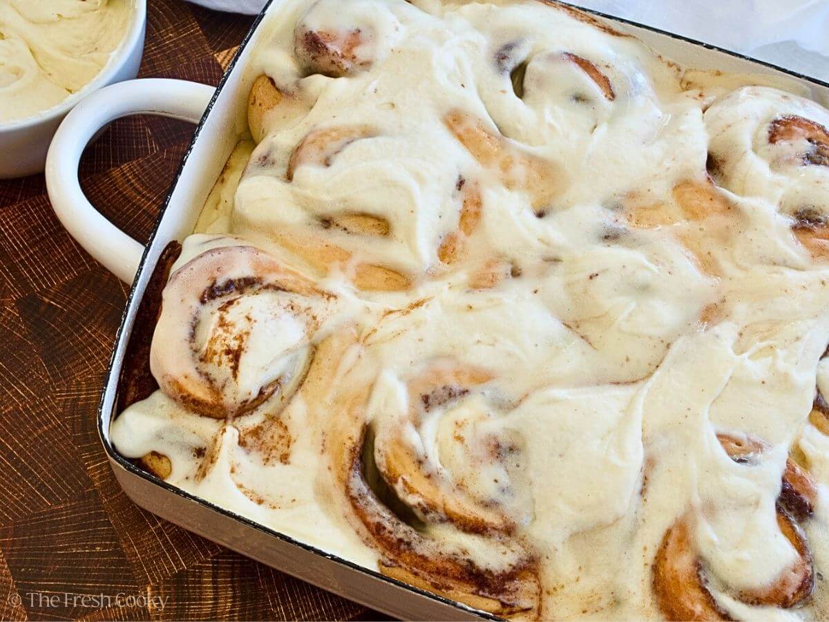 A pan filled with gooey, frosted cinnamon rolls, homemade in a pretty white enameled pan.