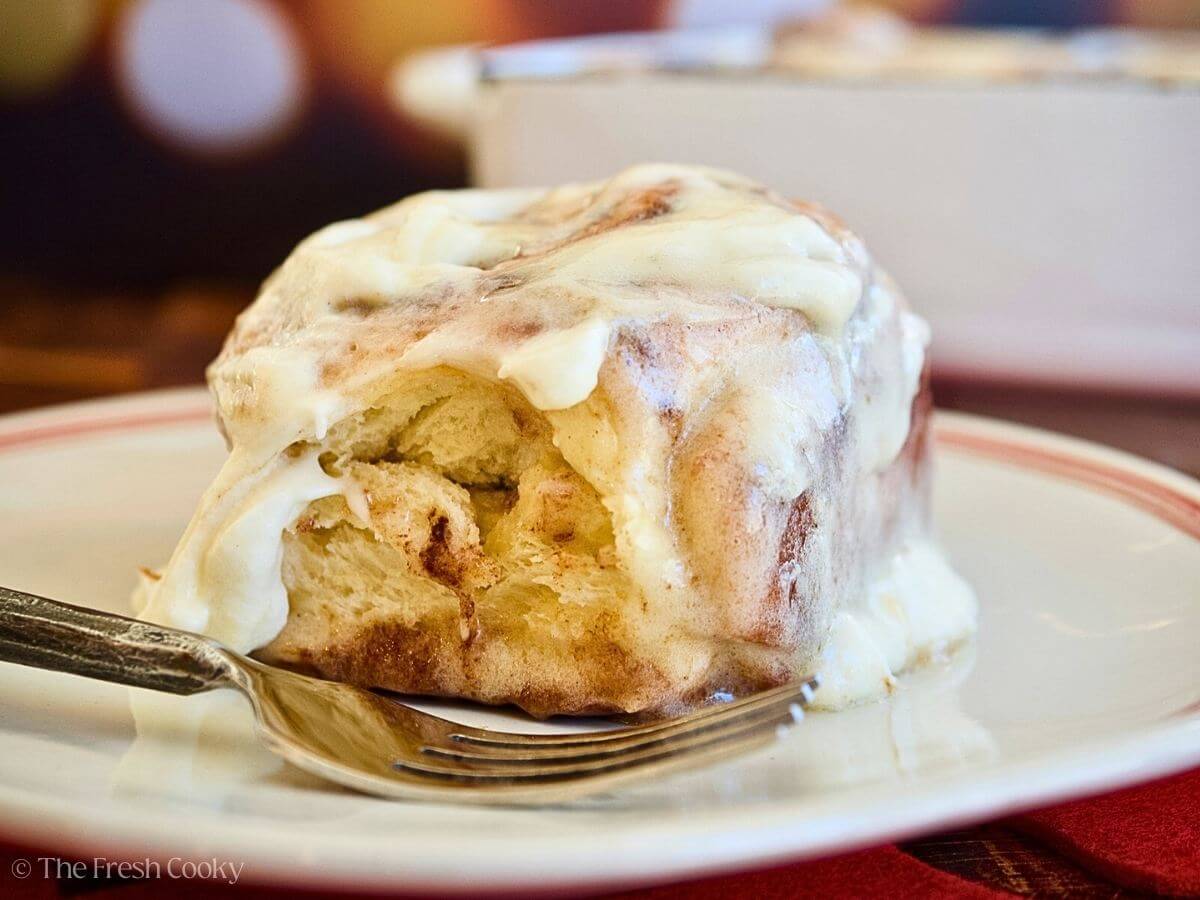 Close up of a gooey cinnamon roll frosted on a plate with a fork.