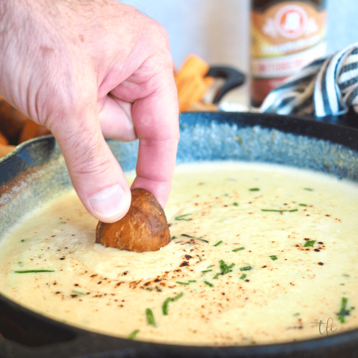 Easy Beer Cheese Dip with hand holding pretzel bite dipping into hot melty cheese dip.