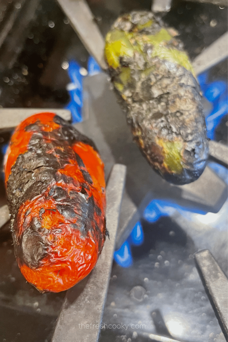 Roasting two jalapenos over an open gas stove flame, charring the skin. 