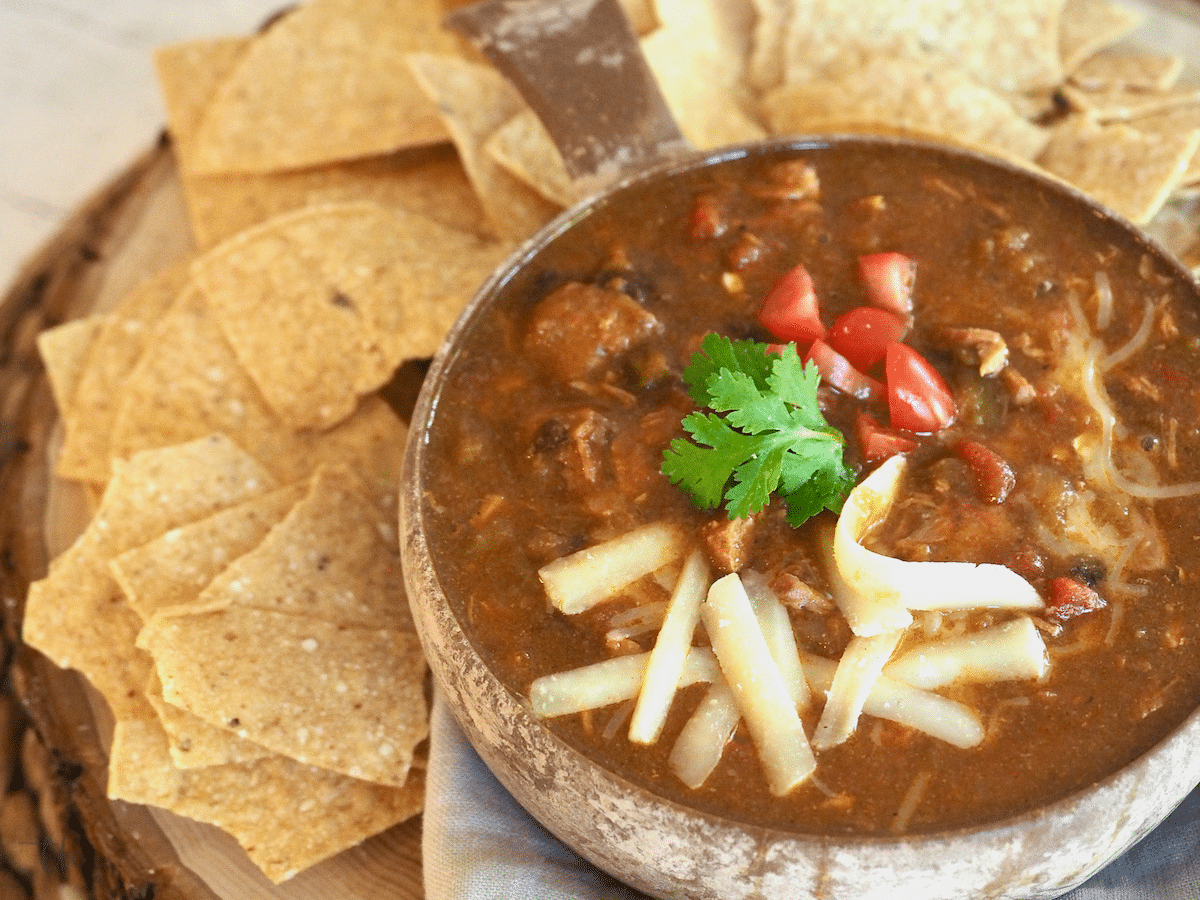 Green chile in bowl with cheese and tortilla chips, ready for dipping.