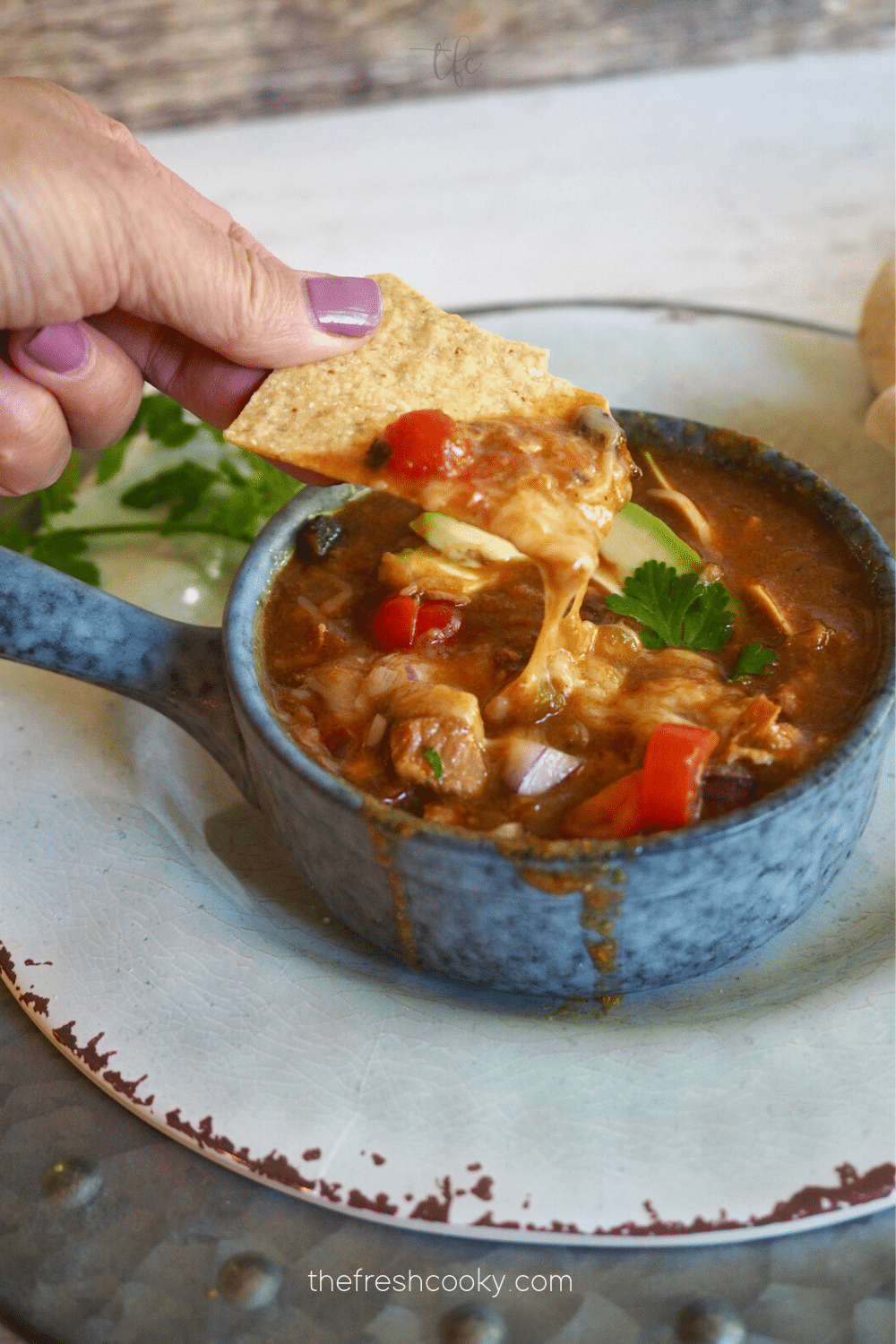 Hand taking bit of green chile verde recipe with tortilla chip dipping in it.