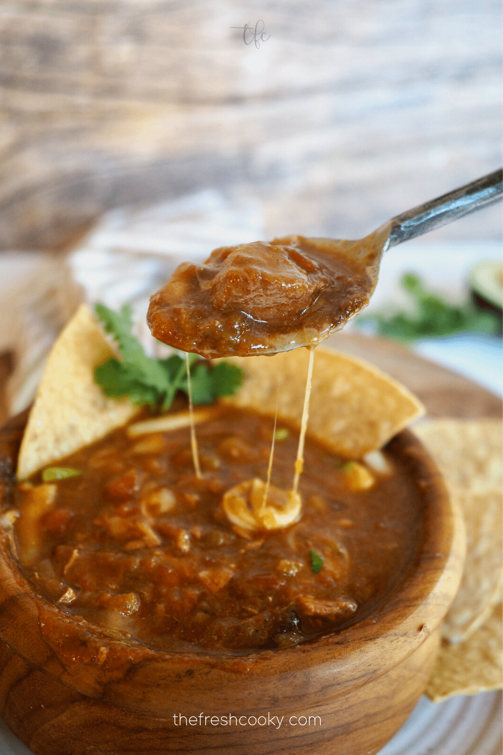 Spoonful of green chile with stringy cheese and chips behind.