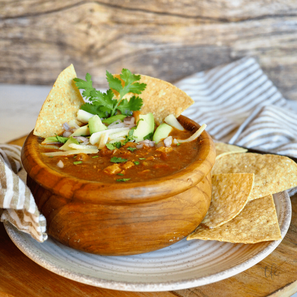 Colorado Green Chili verde in a wooden bowl garnished with tortilla chips, cheese, avocados and cilantro.