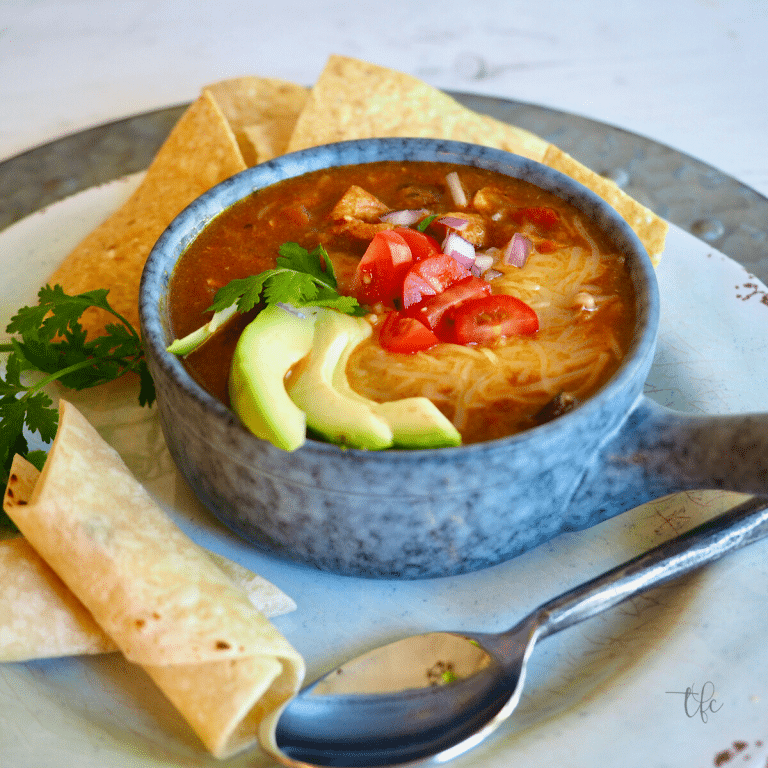 Colorado Green Chili square image chile in soup bowl with sliced avocado, tomatoes, cheese and tortilla chips nearby.