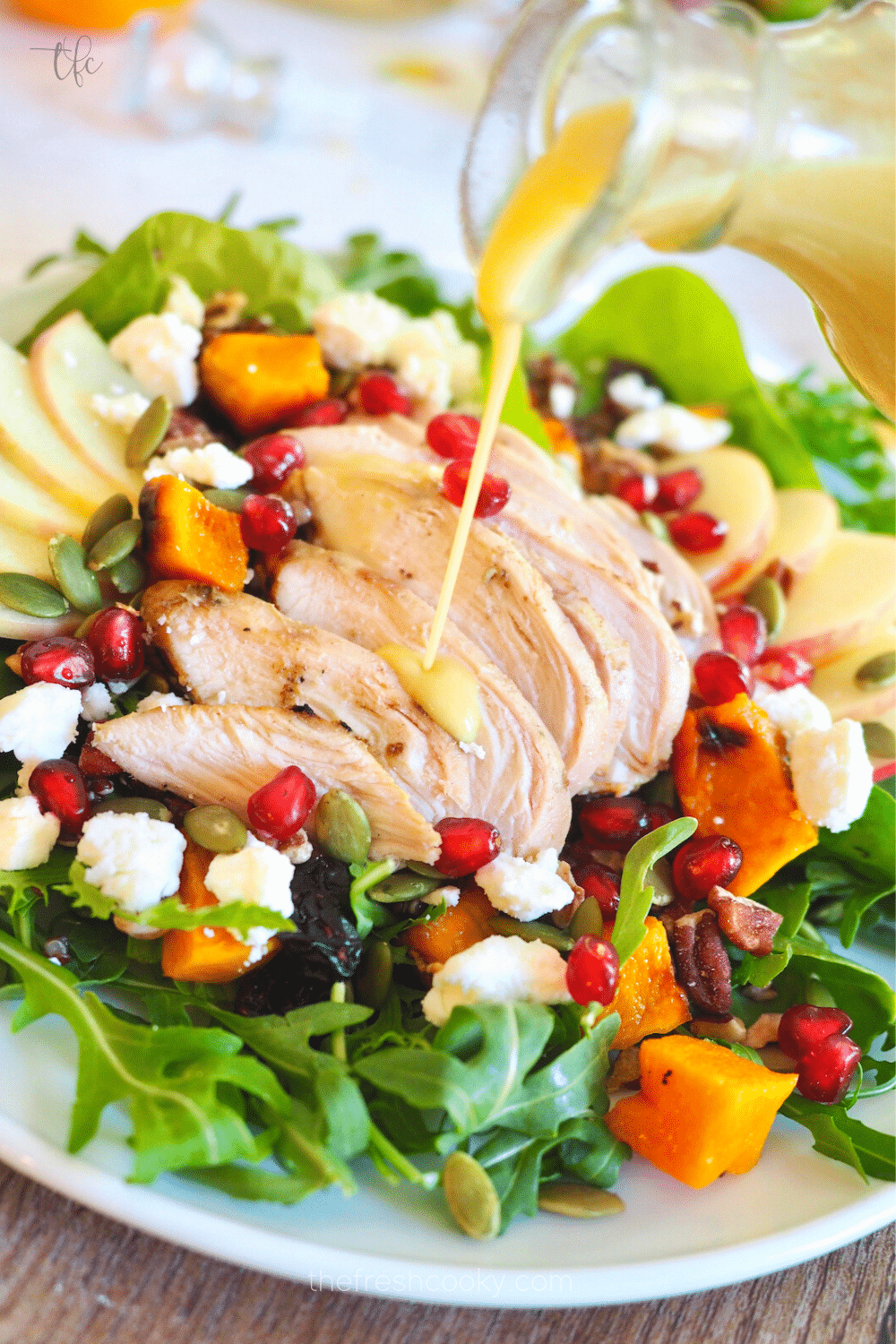 Pouring apple cider vinaigrette over a beautiful salad.