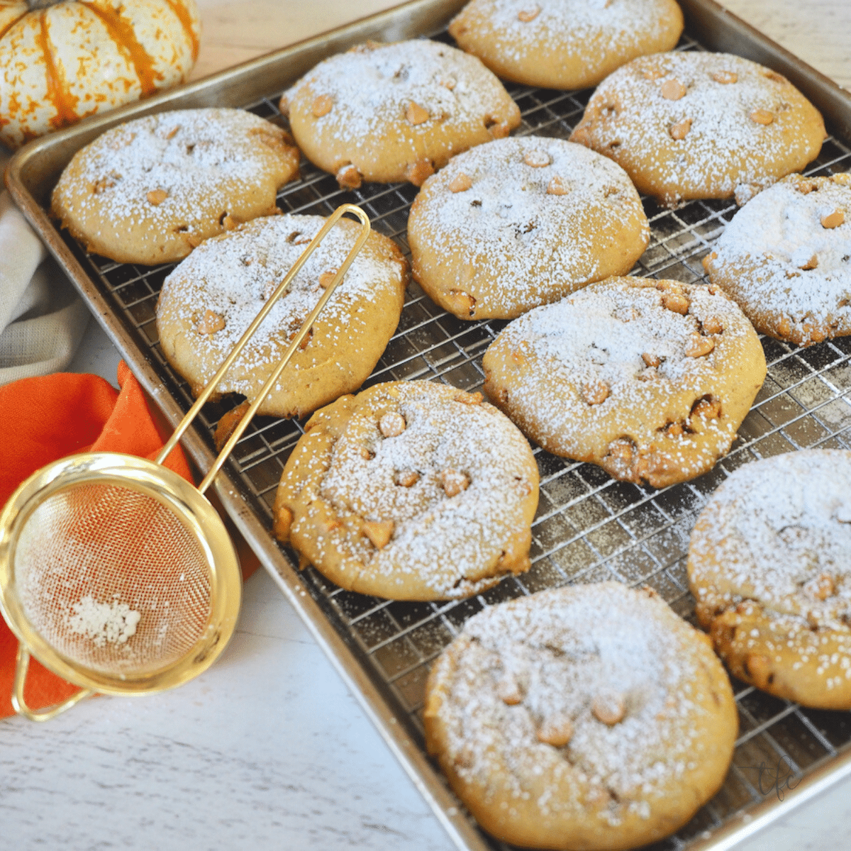 Soft pumpkin cookies with butterscotch chips on cooling rack sprinkled with powdered sugar.