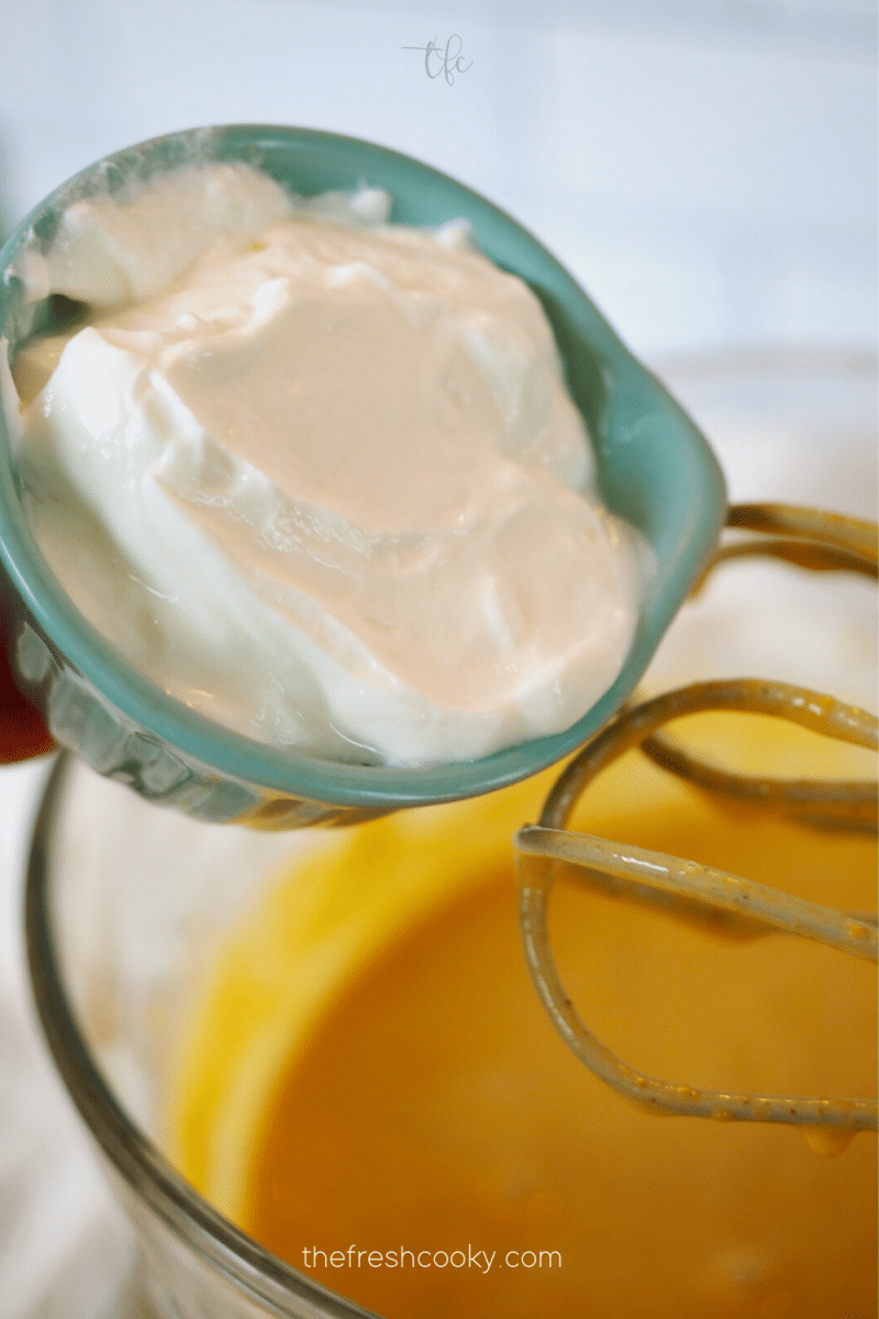 Pouring in Greek yogurt to pumpkin cheesecake mixture.