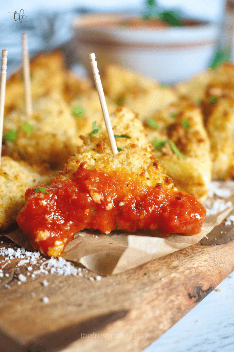 Air Fried toasted ravioli with toothpick in it and dipping into marinara sauce.