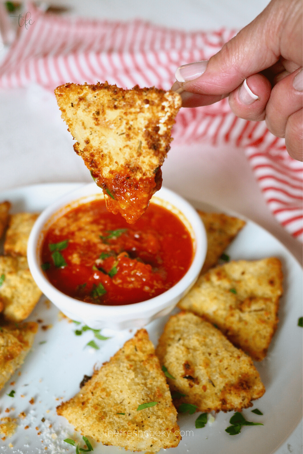 Air Fryer Ravioli with hand dunking toasted ravioli into marinara sauce.