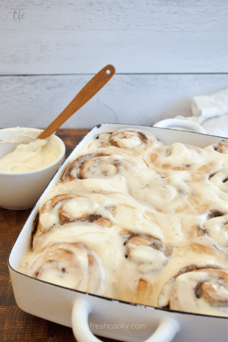 Pan of cream cheese frosted chewy, gooey cinnamon rolls with extra frosting.