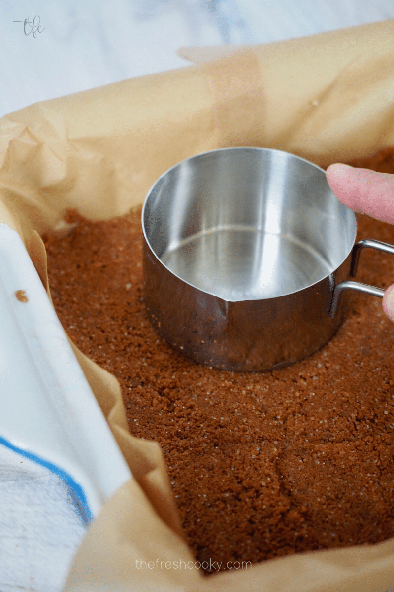 Using measuring cup to firmly press biscoff cookie crust into baking dish. 