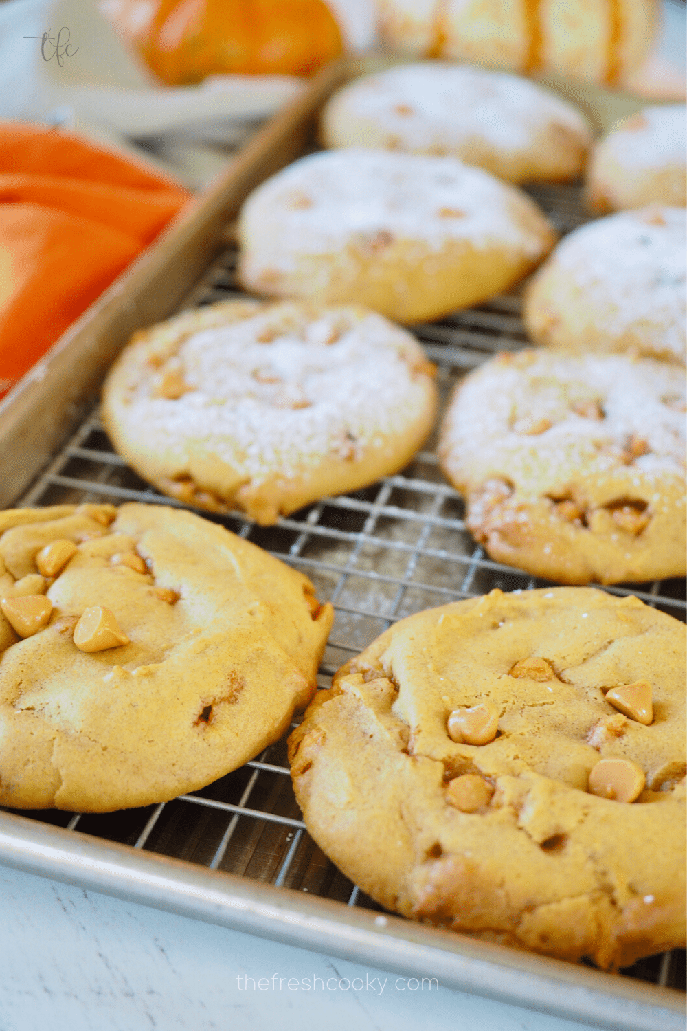 Soft pumpkin cookies with butterscotch chips on wire rack, some with powdered sugar and some without.