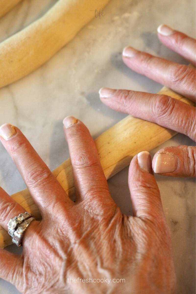 Hands rolling pretzel dough into ropes. 