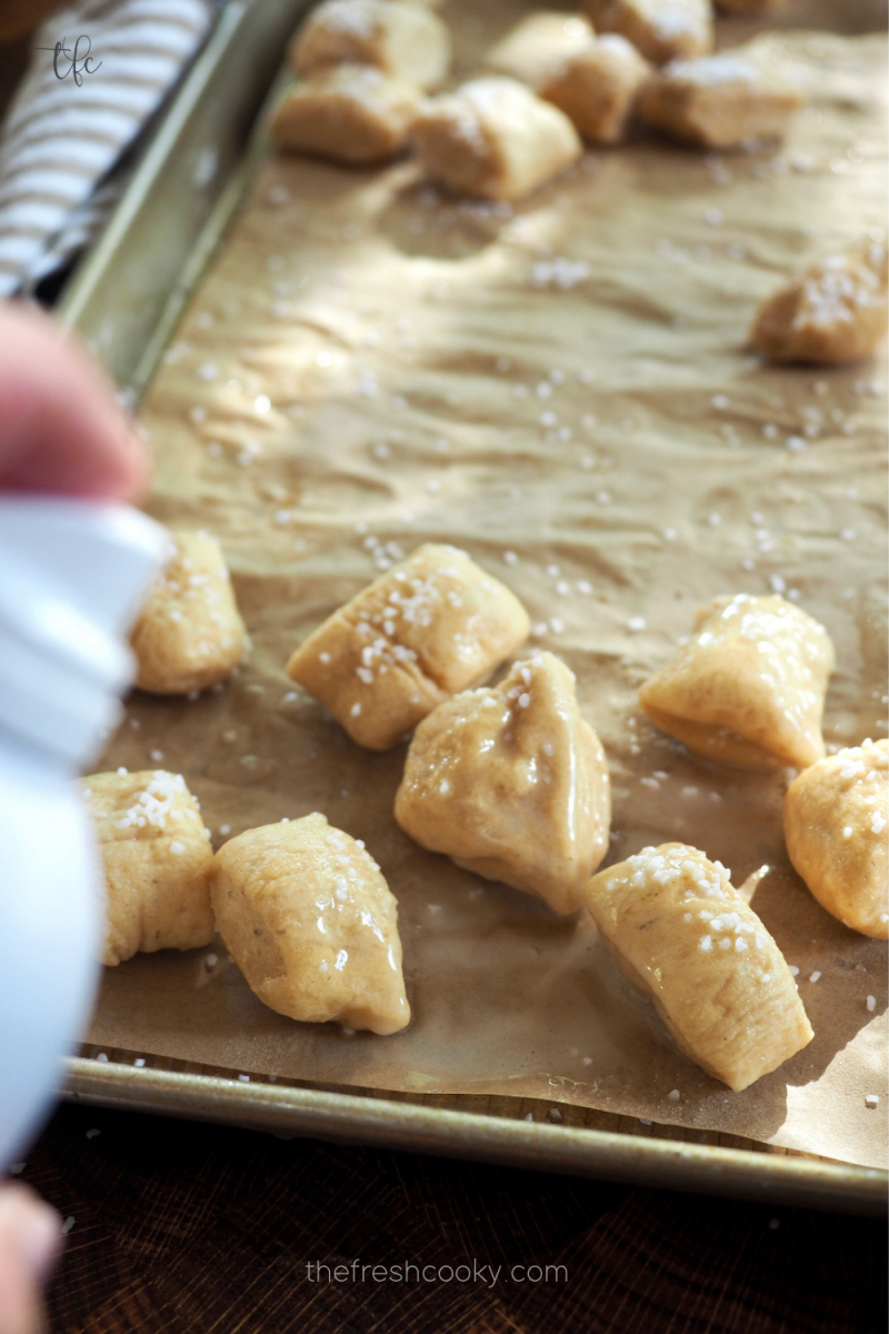 Spraying air fryer pretzel bites with spray oil. 