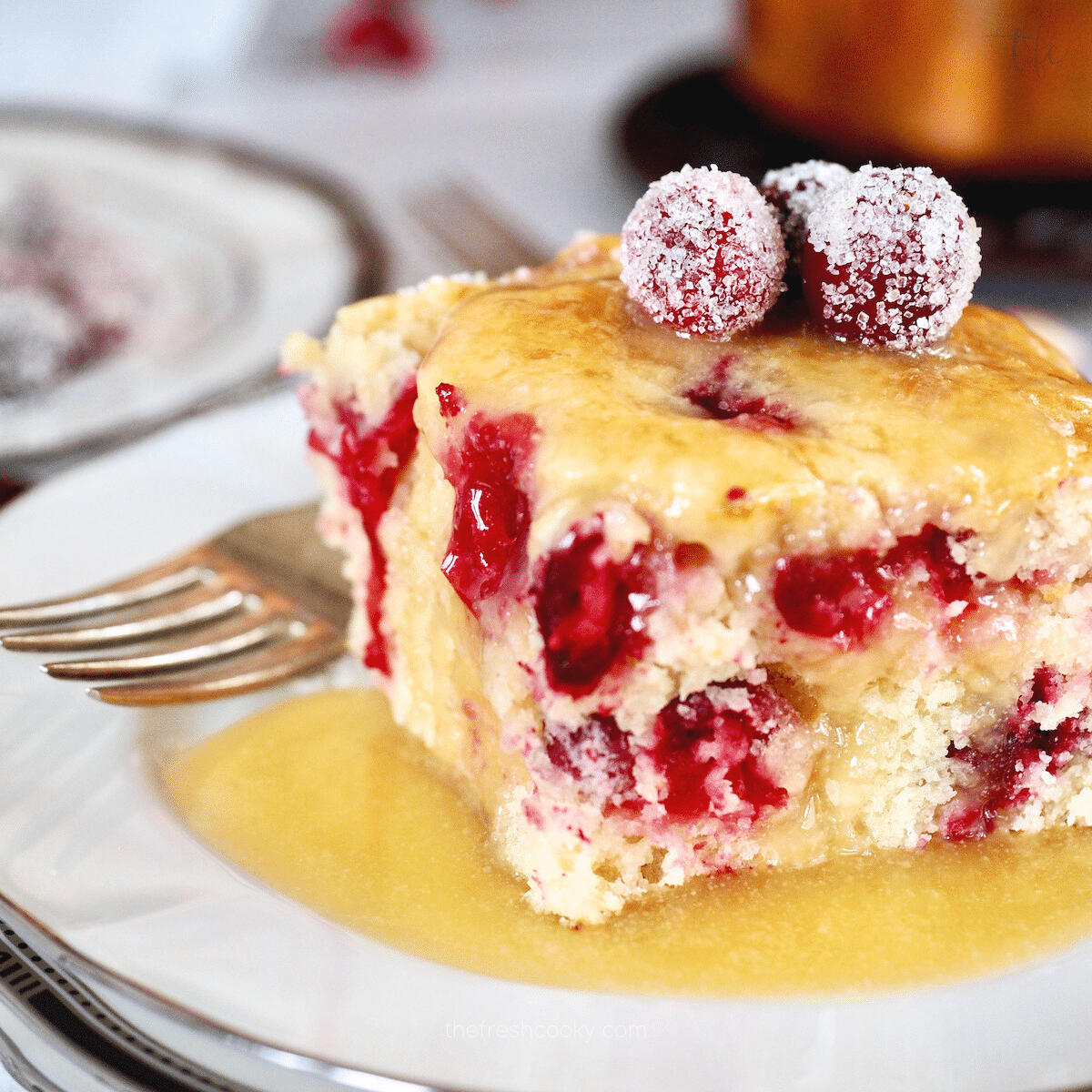 Cranberry Christmas Cake slice on a plate drizzled with vanilla butter sauce and topped with sugared cranberries.