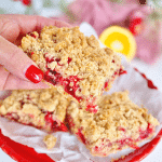 Hand holding a large square of cranberry oatmeal bars with streusel topping.