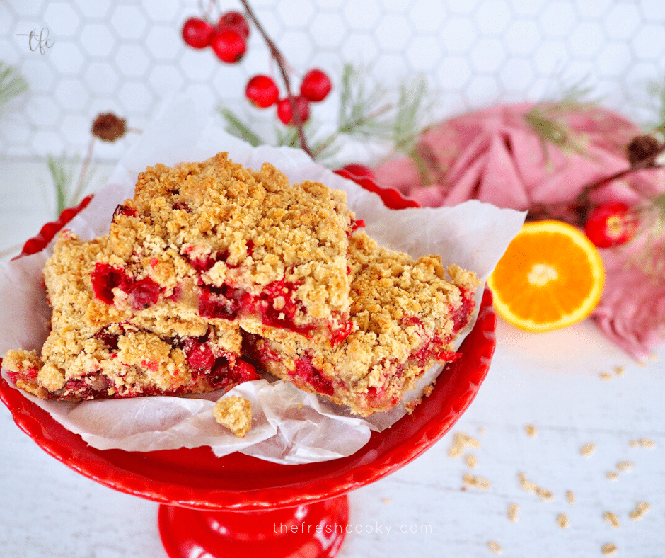 Three Cranberry Oatmeal Bars on a red pedestal plate with an orange and cranberries in the background.