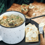 Square image of rustic mug filled with creamy Instant Pot Chicken and Wild Rice Soup, on a black plate with buttered saltine crackers.