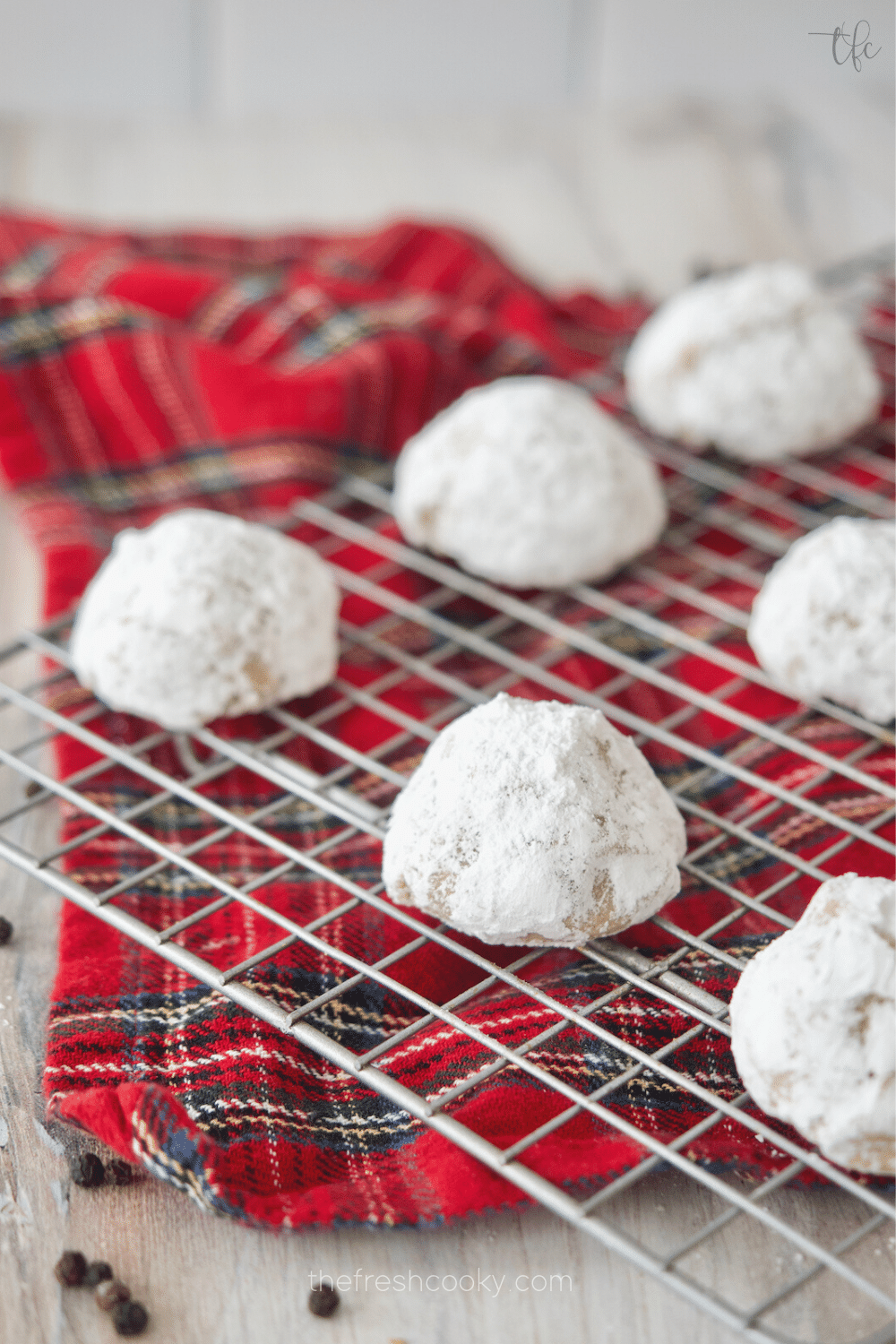 Wire rack holding several pfeffernusse cookies rolled in powdered sugar with a pretty red plaid napkin beneath.