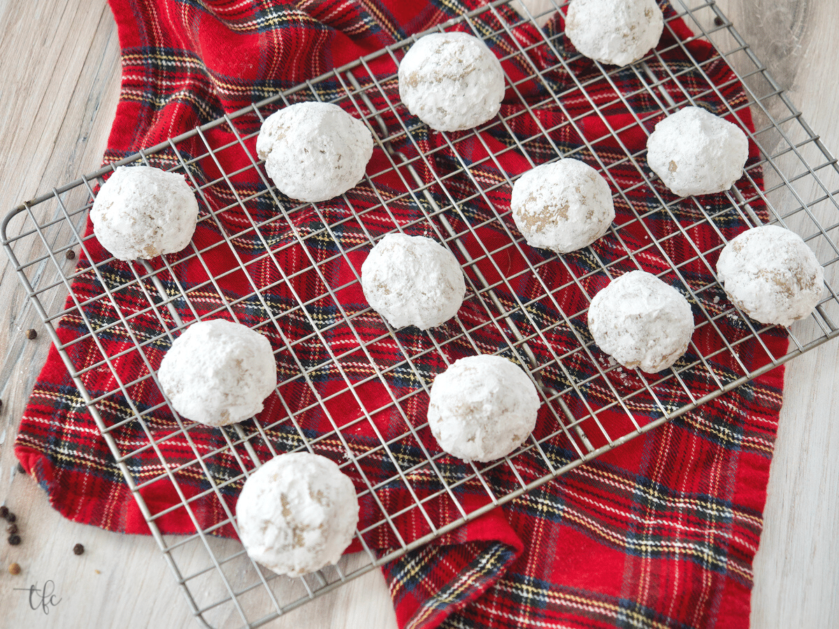 Landscape image of pfeffernusse cookies on a wire rack with a red plaid napkin beneath.