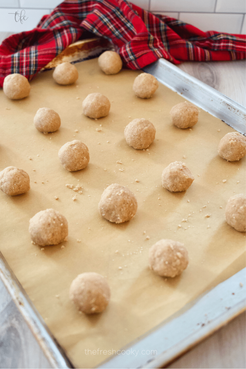 Rolled pfeffernusse cookies on a parchment lined baking sheet ready to bake. 