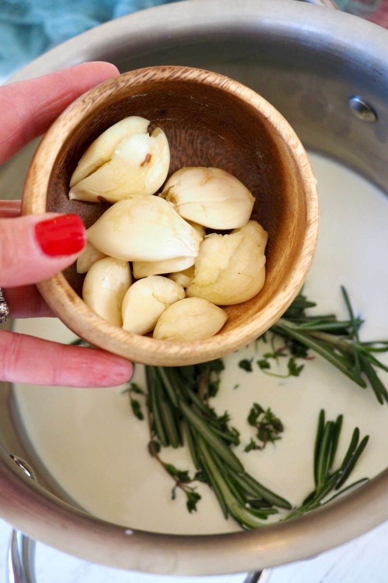 Pouring in fresh, smashed garlic cloves to herb mixture.