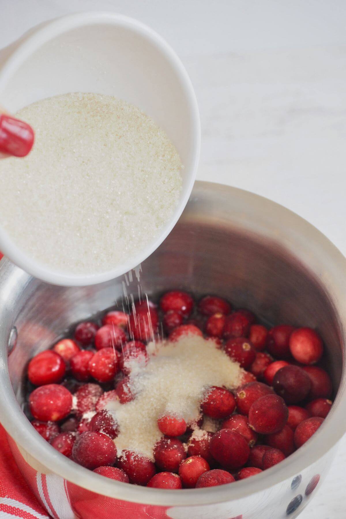 Adding sugar, orange juice and lemon juice to cranberries to make homemade cranberry sauce.