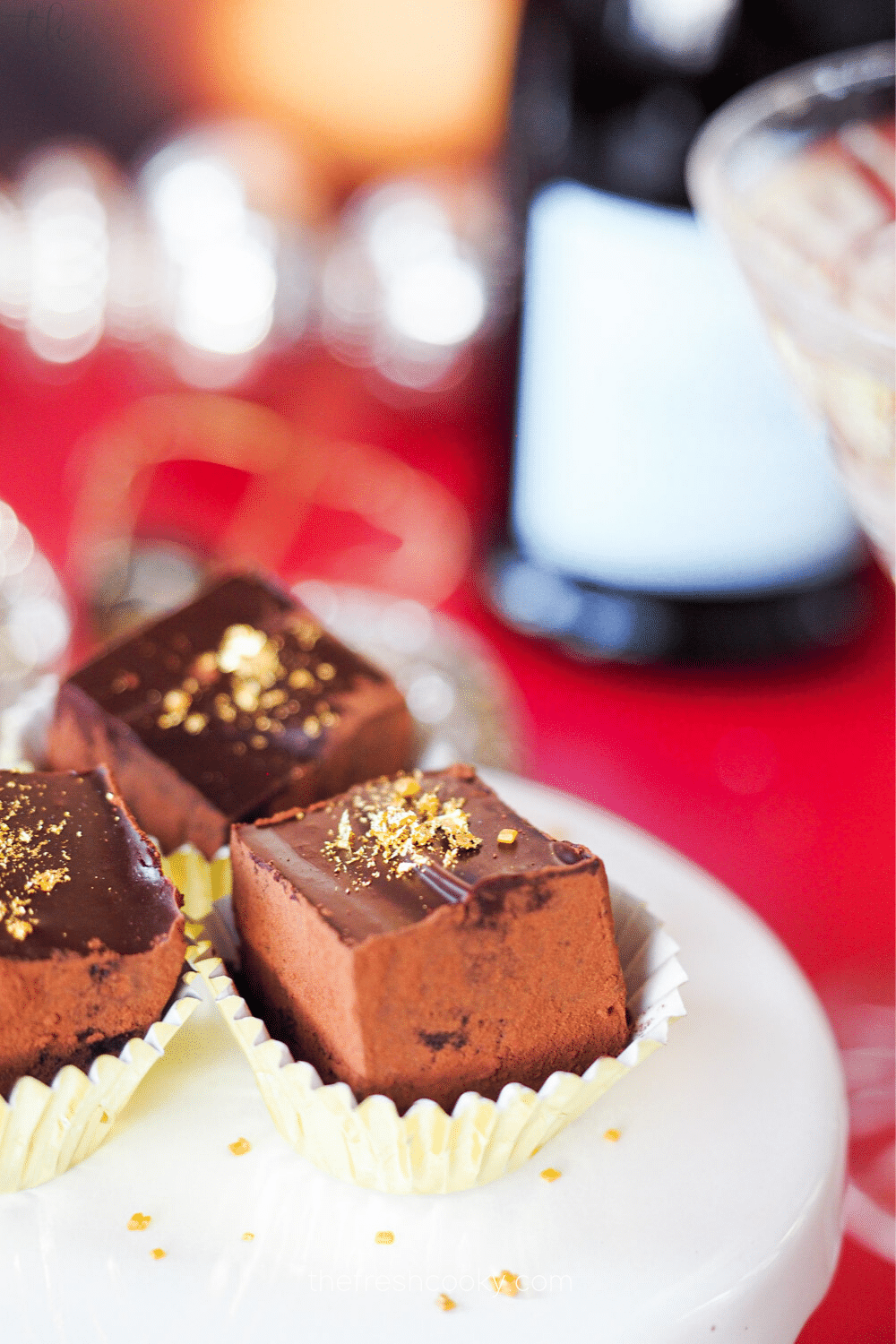 Three champagne truffles in gold baking cups on a white tray with champagne glass and bottle behind.