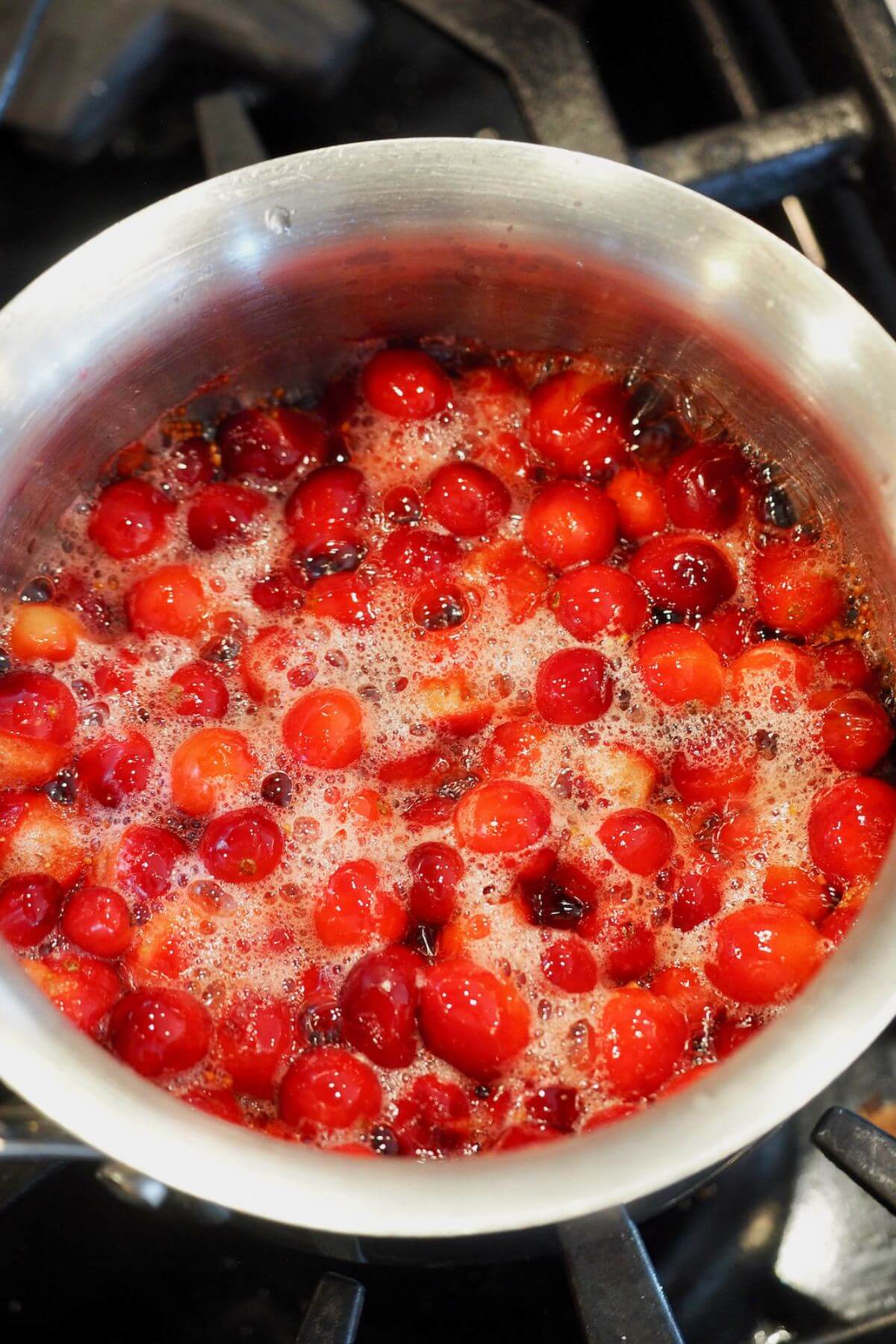 Simmering cranberries on stovetop, cranberries bursting for homemade cranberry sauce.