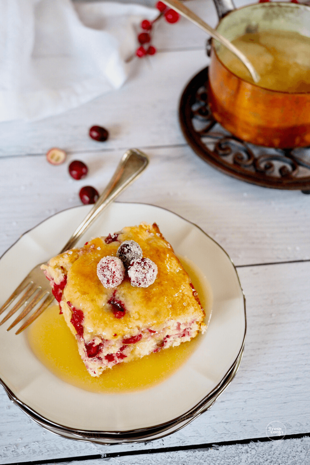 A slice of Christmas cake on a plate drizzled with vanilla sauce and sugared cranberries.