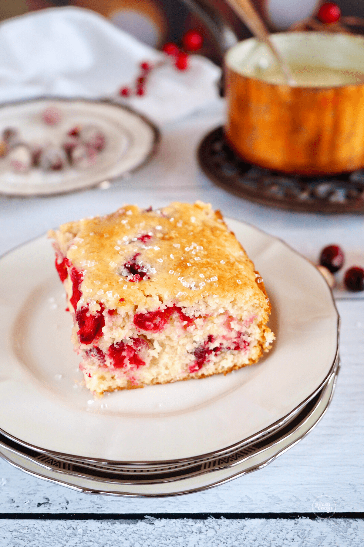 Serving of cranberry christmas cake on plate with butter sauce in background.