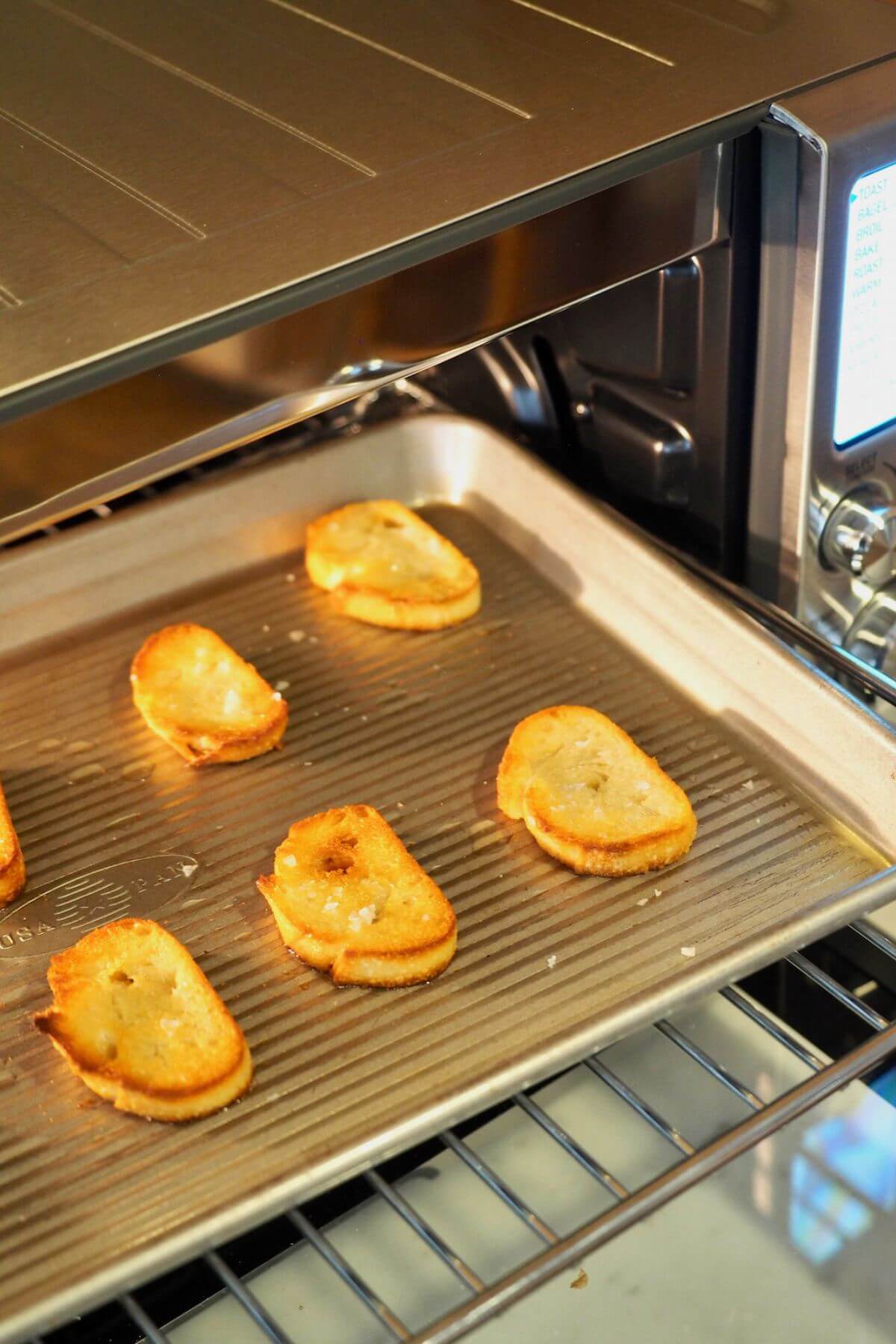 Placing tray of baguette slices into Breville Smart oven for toasting.