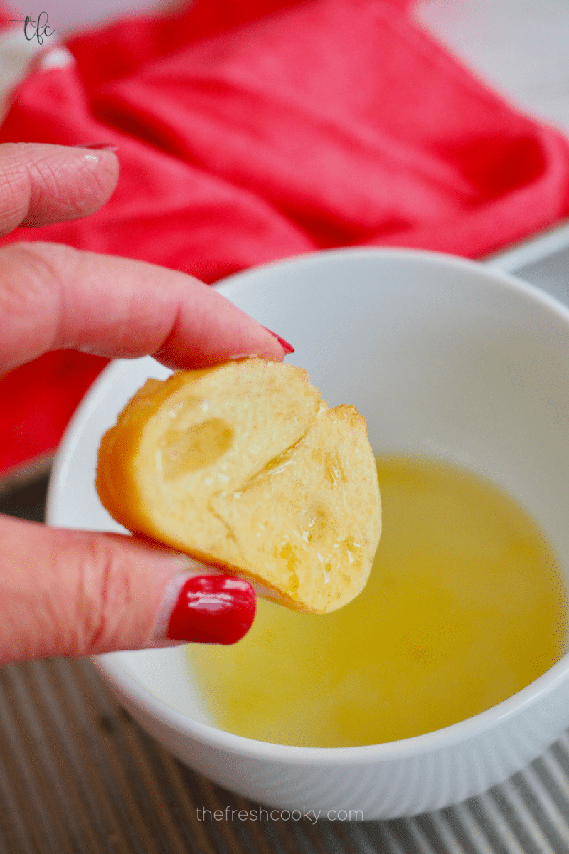 Lightly dipping baguette slice into olive oil for crostini. 