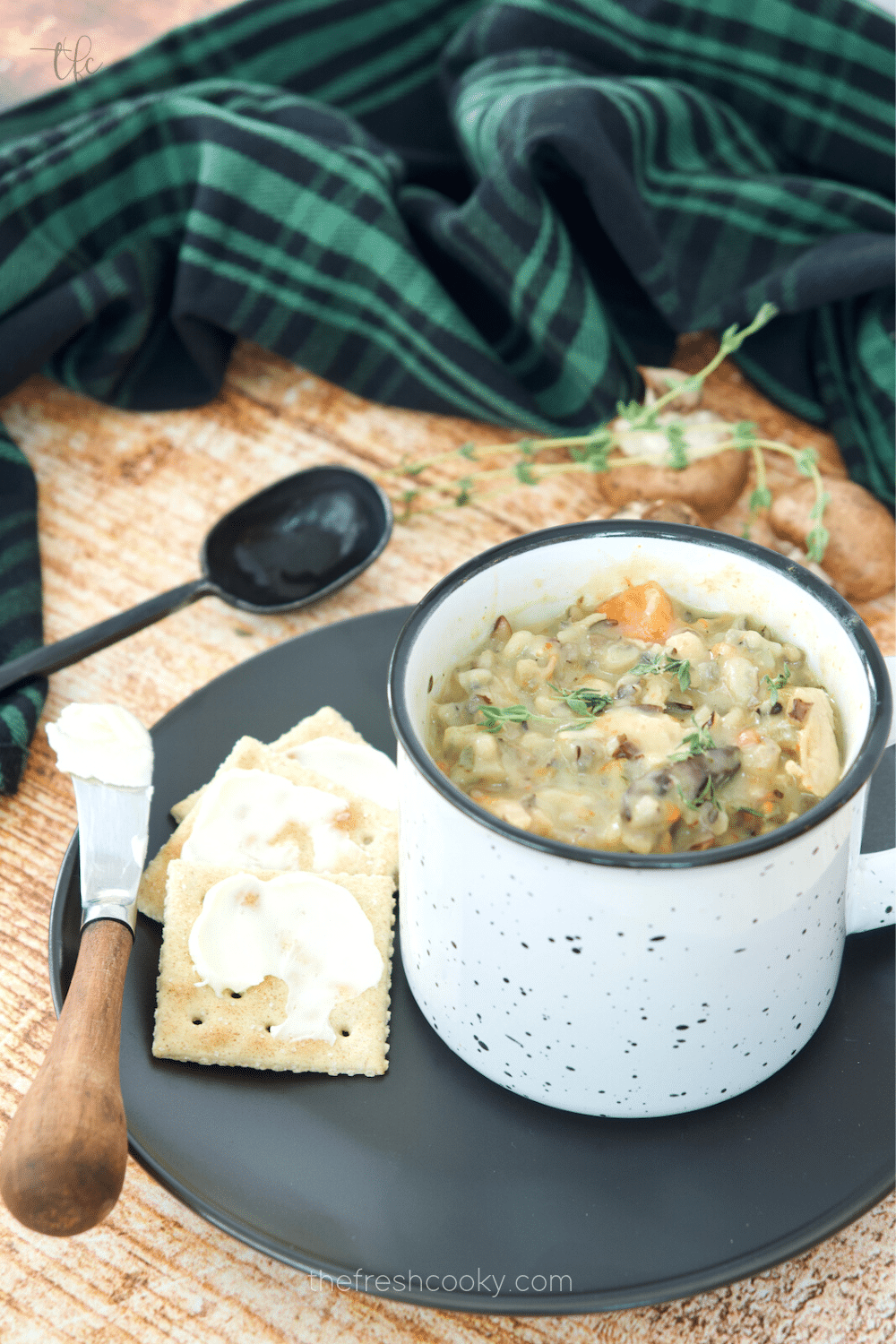 Mug filled with Instant Pot Chicken and Wild Rice Soup on a plate with buttered saltines.