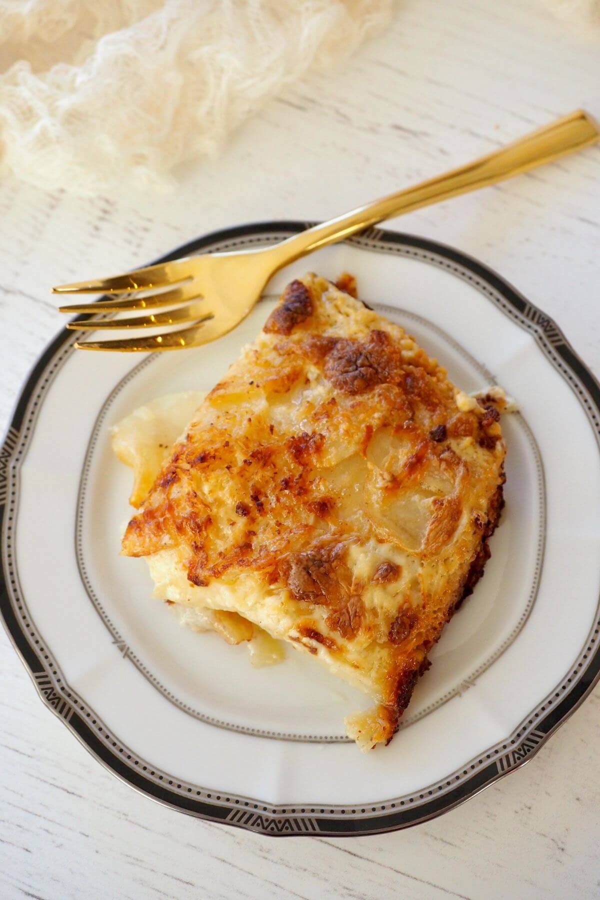 Slice of potatoes dauphinoise on plate with gold fork.