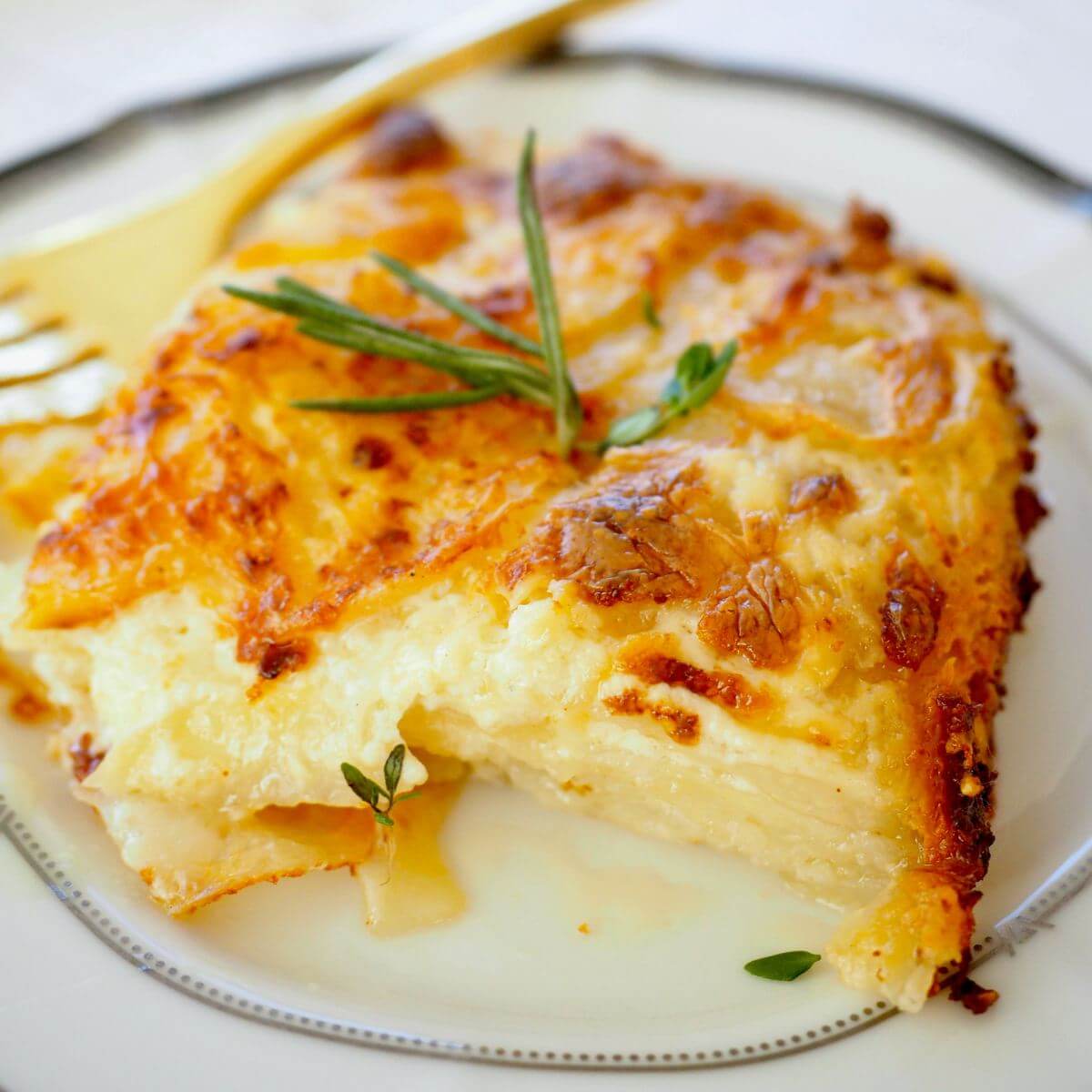 A slice of potatoes au gratin on a plate topped with a sprig of thyme and rosemary. 