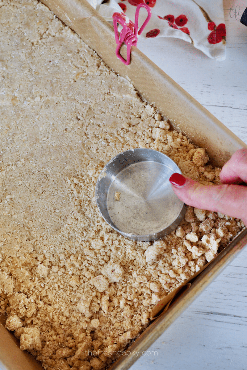 Pressing crumb mixture into prepared pan for oatmeal cranberry crumb bars. 