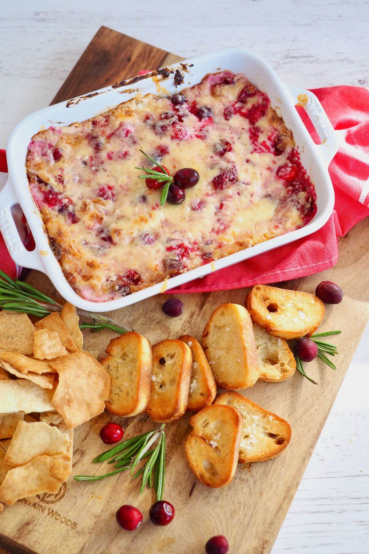 Cream cheese cranberry hot dip on board with crostini and pita chips.
