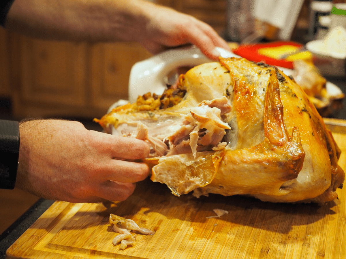 Male hands, carving a turkey on a cutting board.